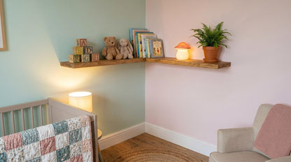 Two wooden corner shelves on a light green and pink wall