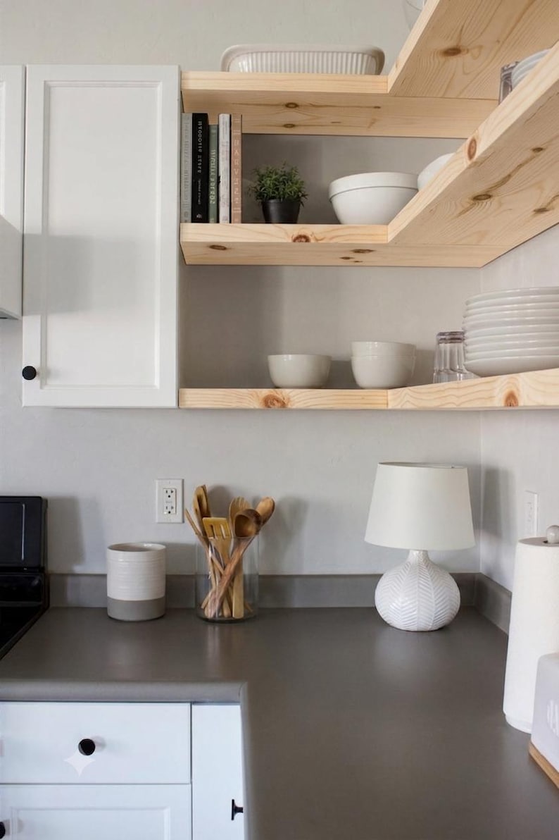 Light wood floating corner shelves next to white kitchen cabinets