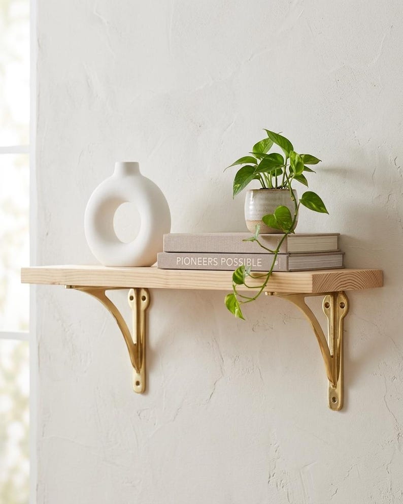 Natural wood shelf supported by two polished brass brackets