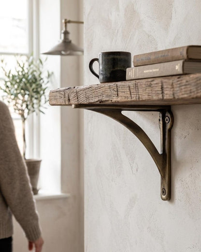Rustic wooden shelf on a dark brass-toned bracket holding a mug and two books