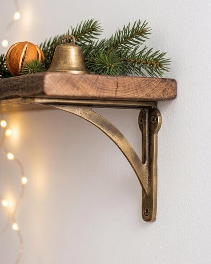 Rustic wooden shelf on a curved antique brass bracket with pine needles, a bell and a dried orange slice