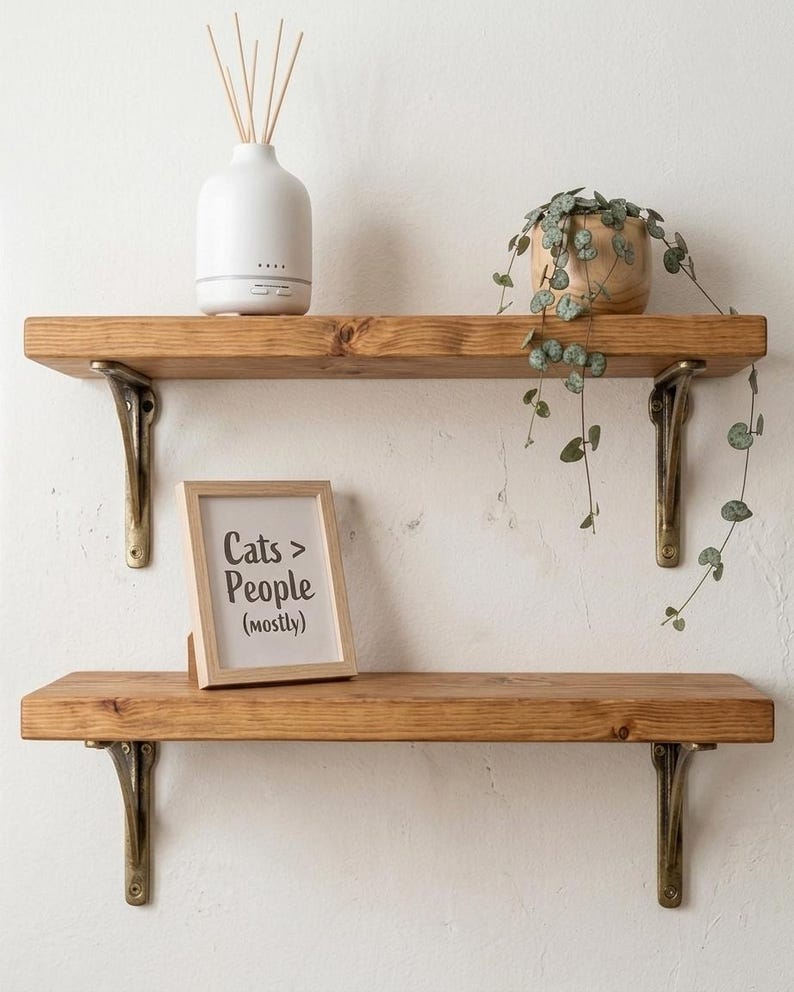 Two wooden shelves on dark metal brackets holding a reed diffuser and a potted plant