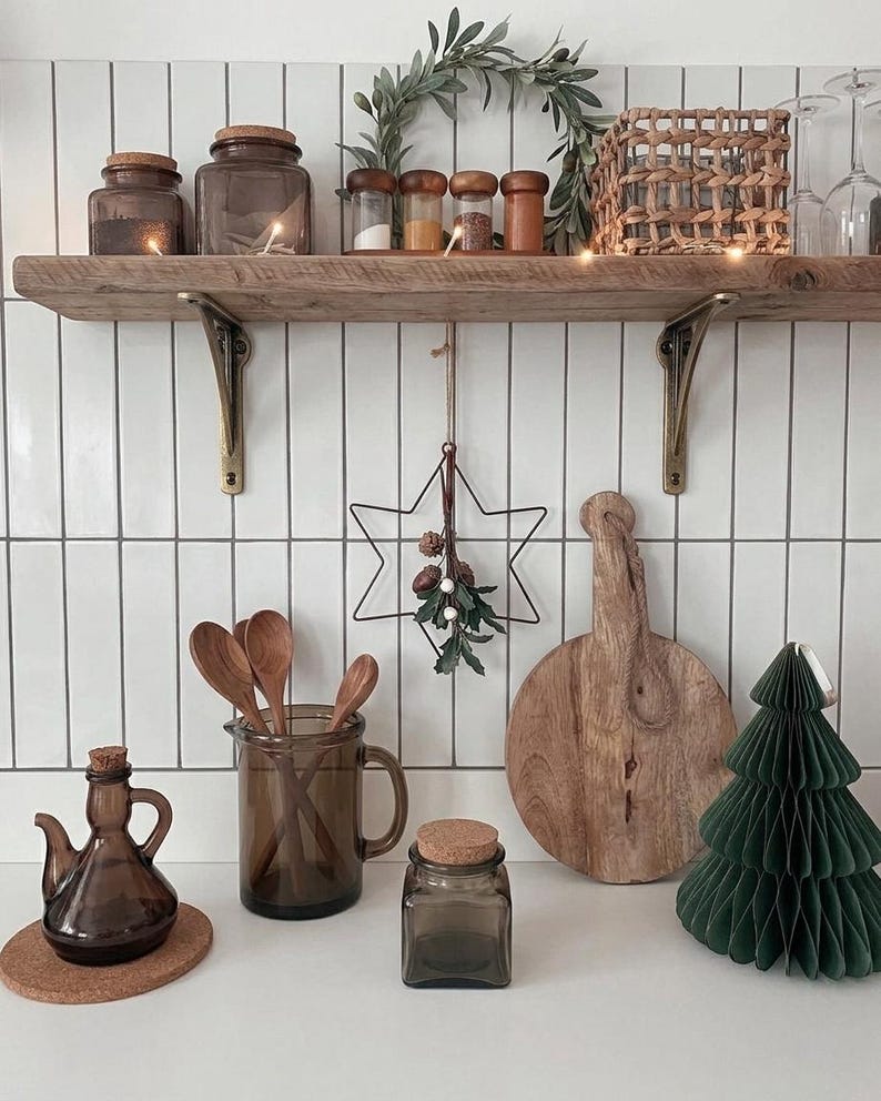 Rustic wooden wall shelf on metal brackets holding glass jars, spice containers and a woven basket