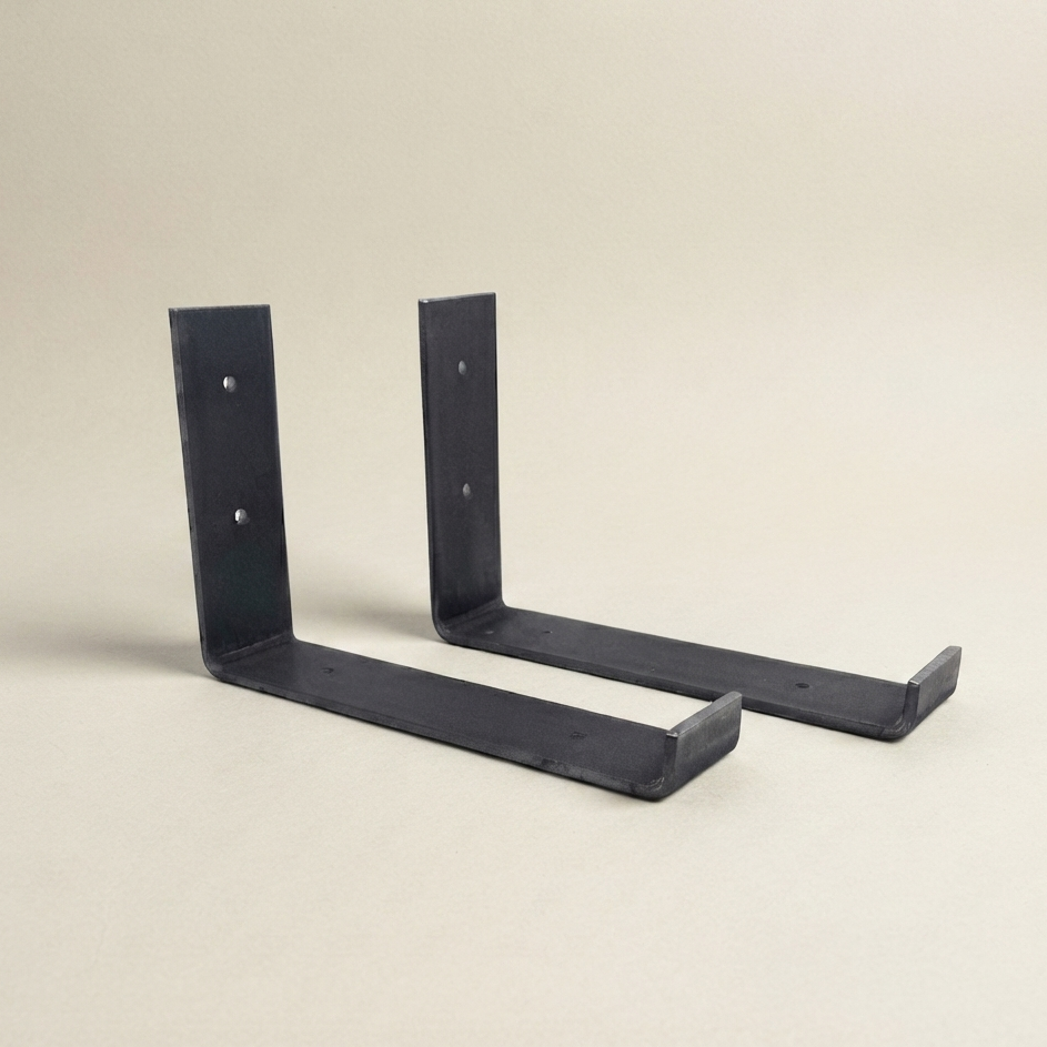Two black metal L-bracket wall mounts shown on a plain beige studio background.