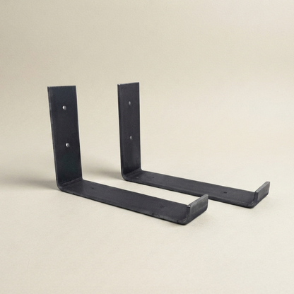 Two black metal L-bracket wall mounts shown on a plain beige studio background.